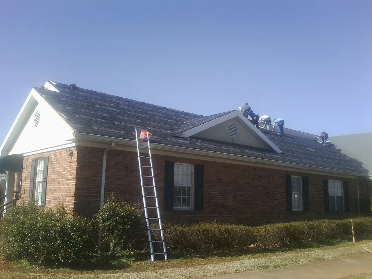 Crew tearing shingles off a brick ranch roof with a ladder set — Emergency Roof Repair work by our crew in Hooper