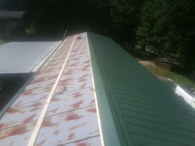 Old rusted panels beside newly installed green metal roofing — Wind Damage Roof Repair by Roofing Brothers in Hooper