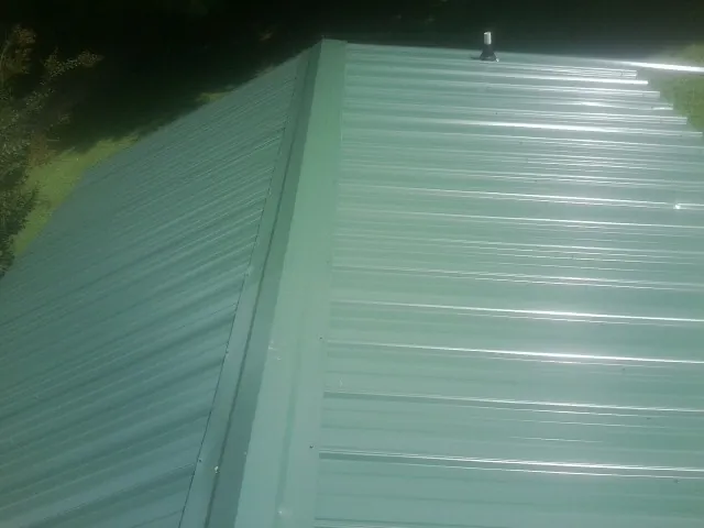 New green metal panels meeting at the ridge of a roof — Flat Roof Repair work by our crew in Hooper