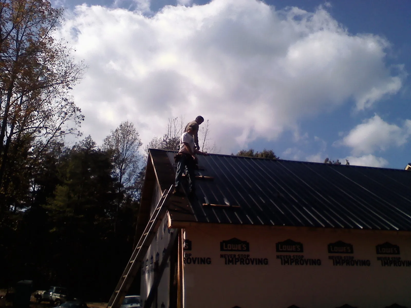 Roofer fastening dark metal panels high against a cloudy sky, from a Roof Inspection job in Hooper